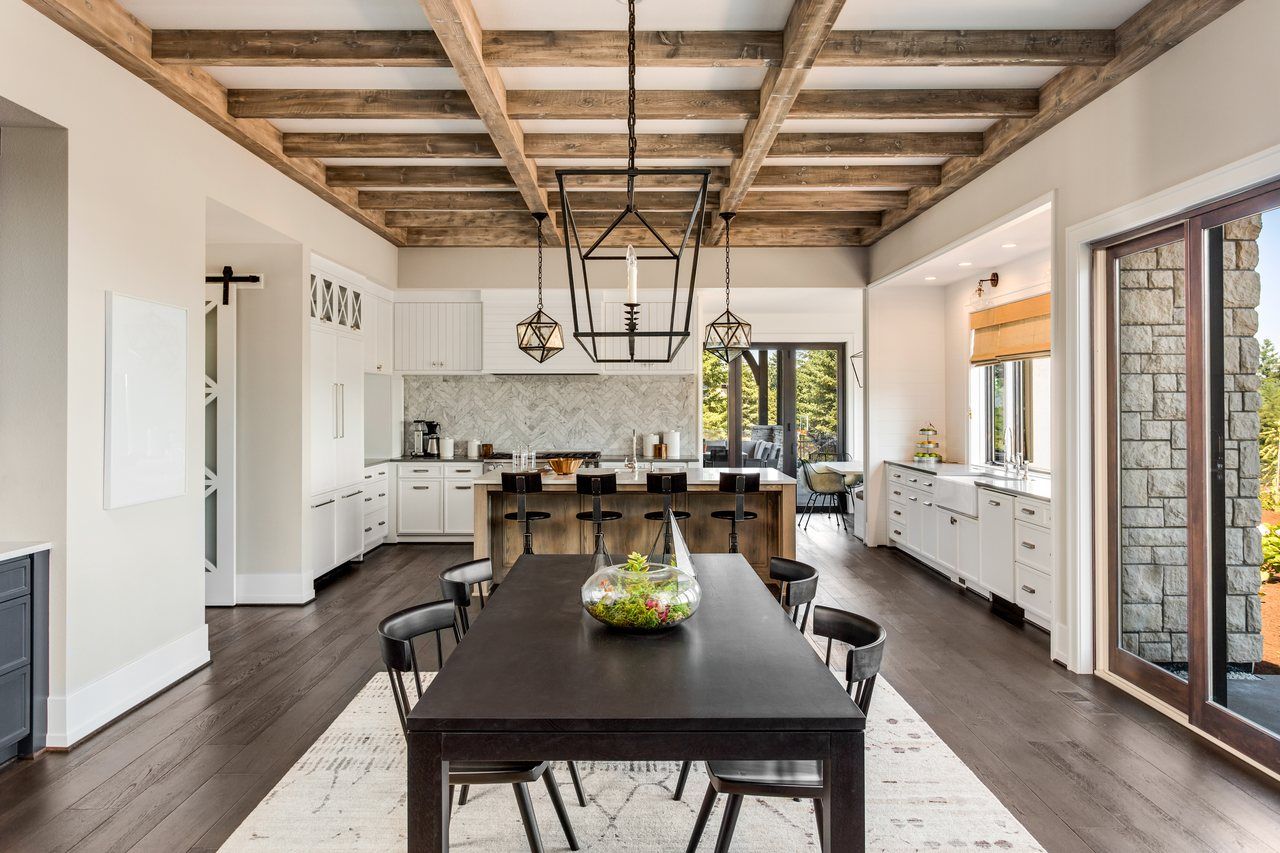 Open-concept kitchen and dining room in a new construction home in Shawnee, KS, with a wood-beamed ceiling, white cabinetry, a wood island, and stone accents